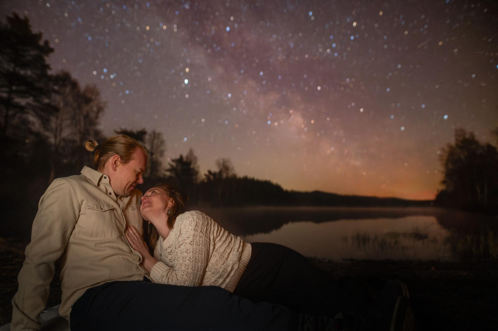 A couple by a still lake under the Milky Way and a starry sky on an astro outing