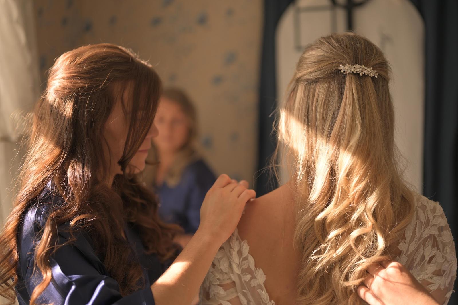 The bride's friend helping with the wedding dress in the morning light during the preparations