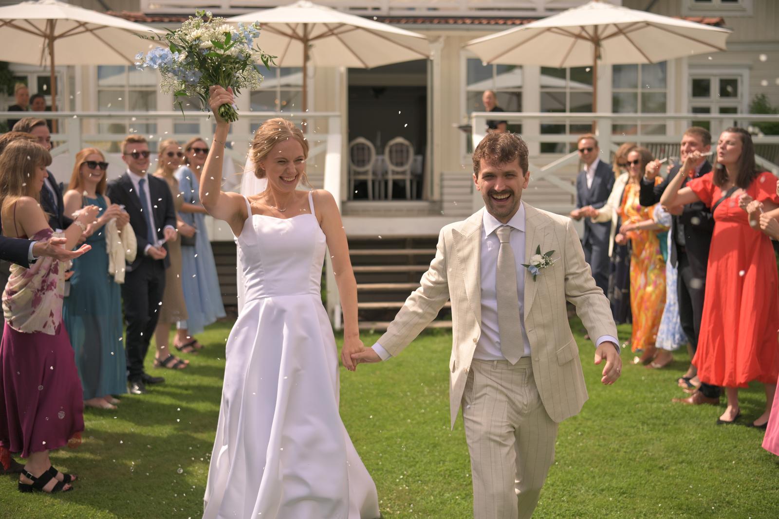 Unedited photo: newlyweds walking hand in hand through cheering guests after the ceremony