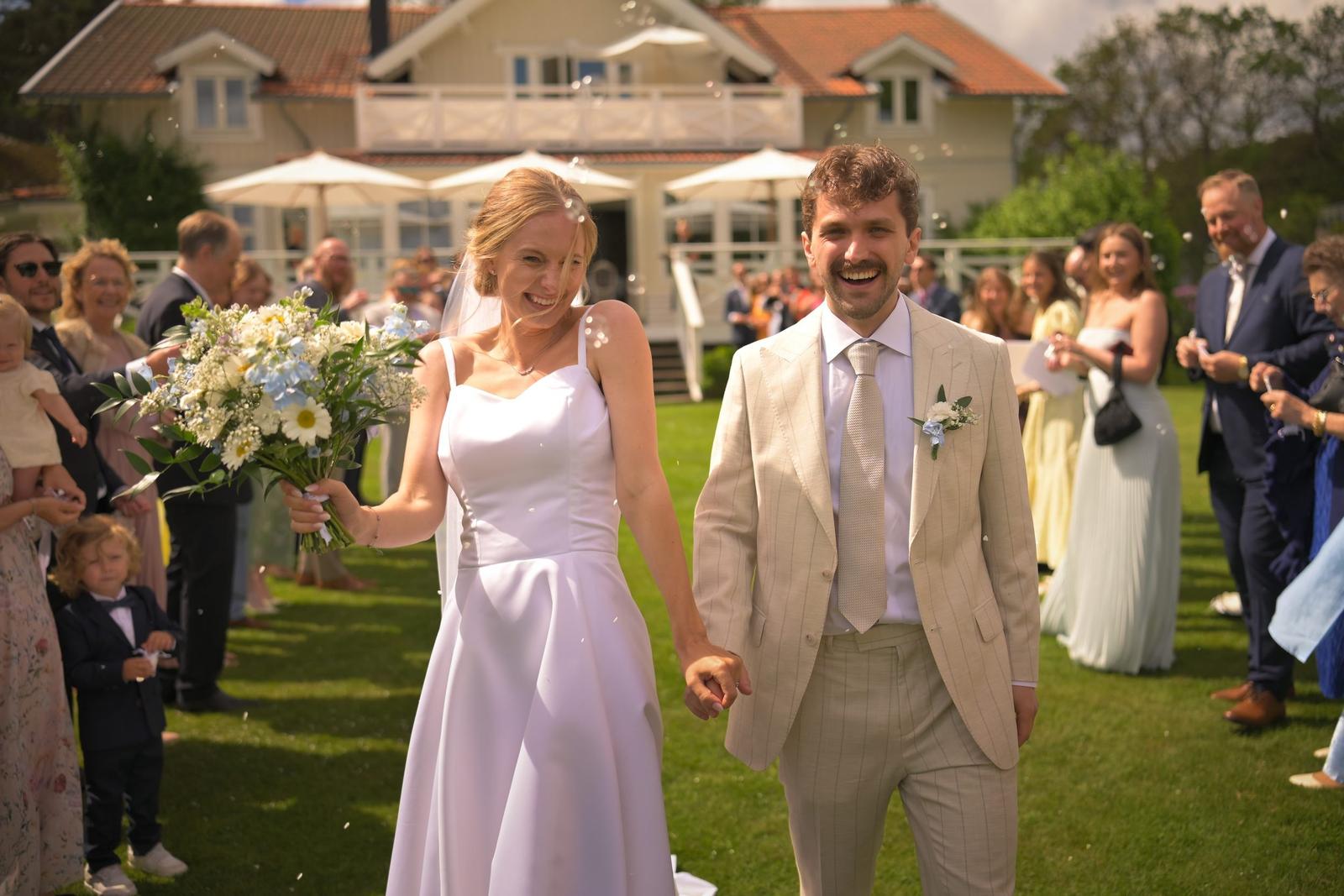 Newlyweds walking hand in hand through cheering guests after the ceremony on the lawn in front of Villa Vanahem in Stenungsund