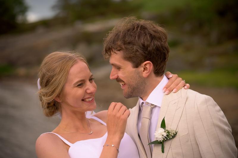 The bride and groom laughing together in a close-up portrait by the water