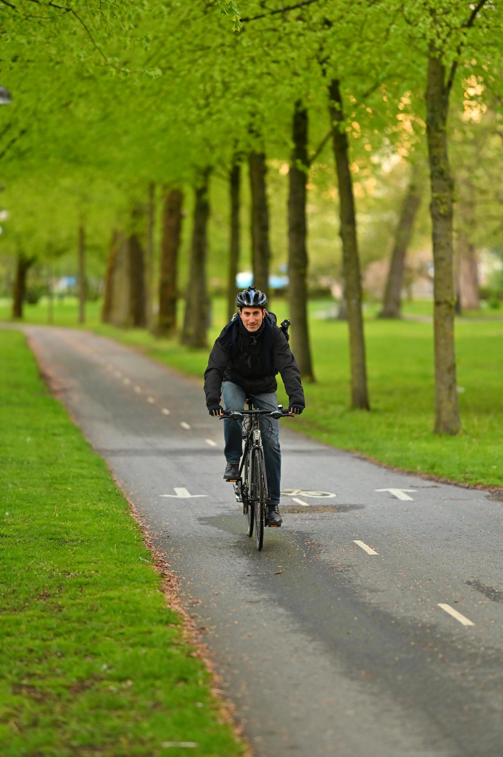 A man riding a bicycle on a tree-lined park pathway during daytime.