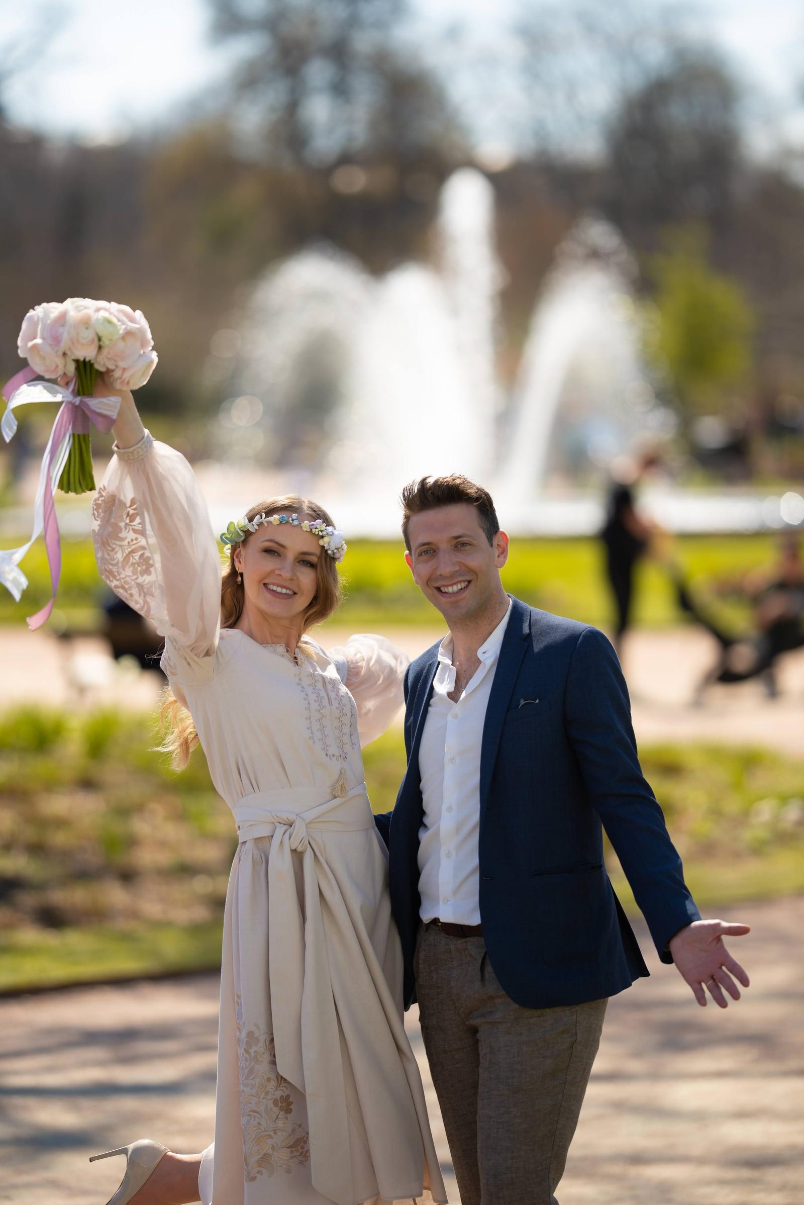 Bride and groom celebrating in front of a fountain in a park while the bride lifts her bouquet
