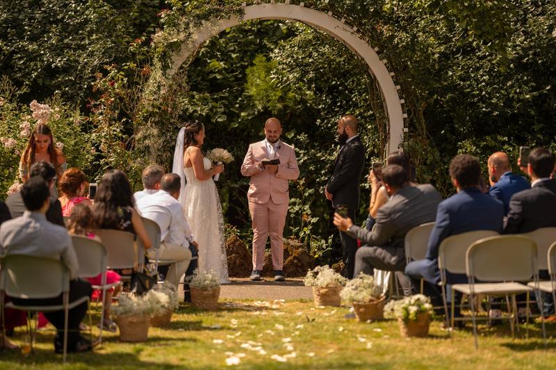 An outdoor ceremony under a white floral arch with guests seated in the garden