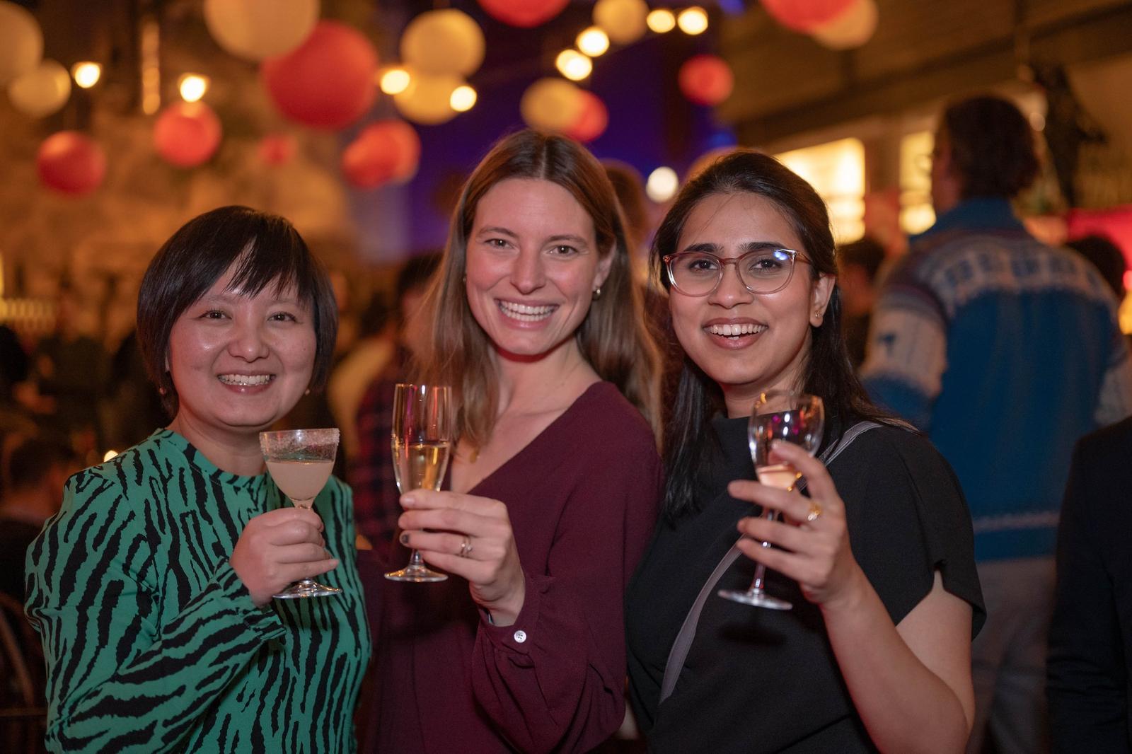 Events: three guests raising their glasses and smiling under colourful lanterns at a party