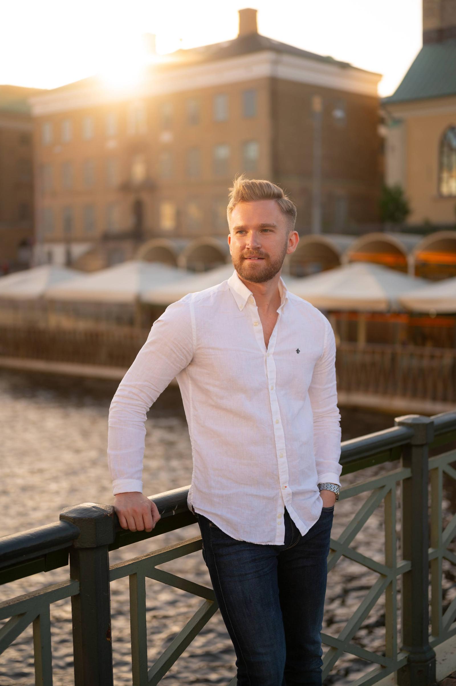 Portraits: a man in a white shirt leaning against a railing in the evening sun