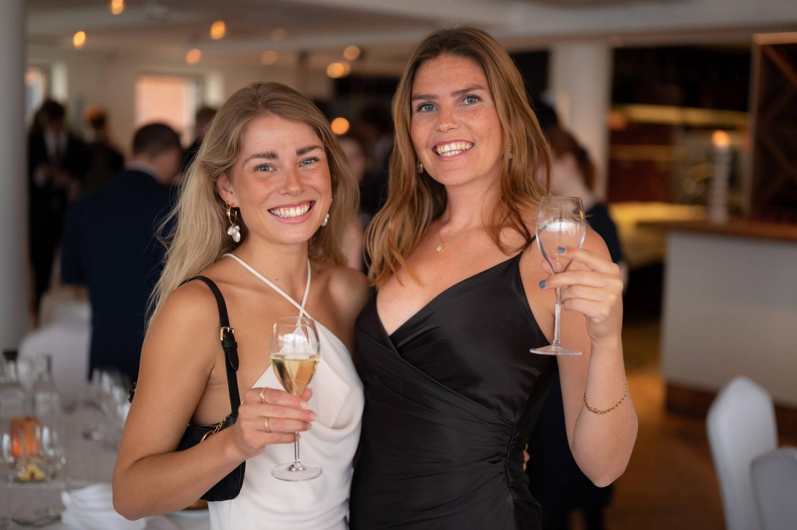 Two women smiling and holding champagne glasses at a social event or party.