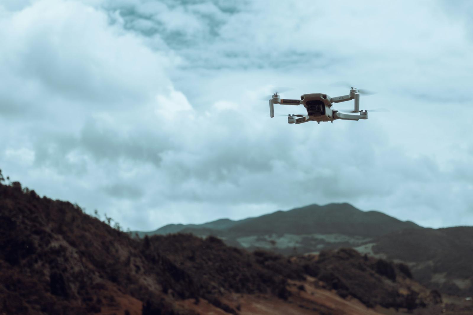 A drone flying over a mountain landscape under a cloudy sky.